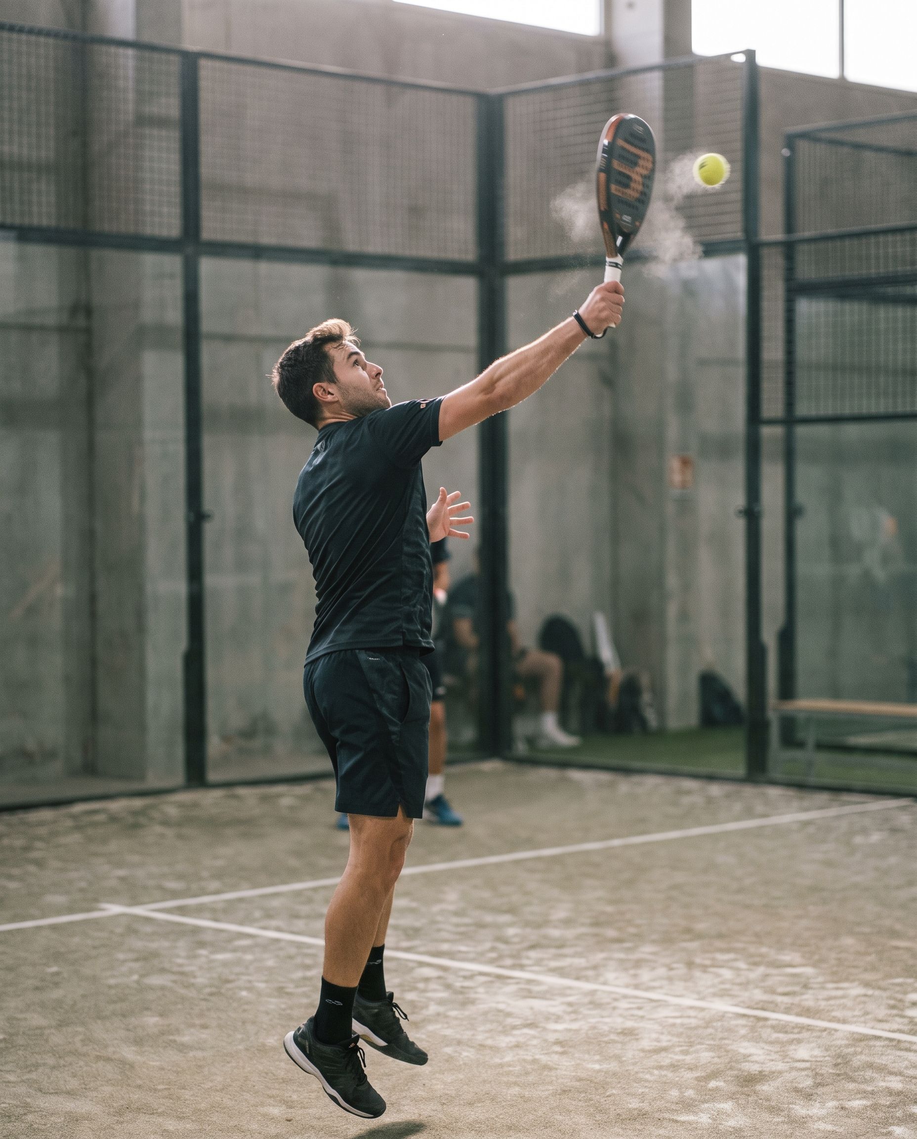 A padel player reaching up for an overhead on a glass-walled court